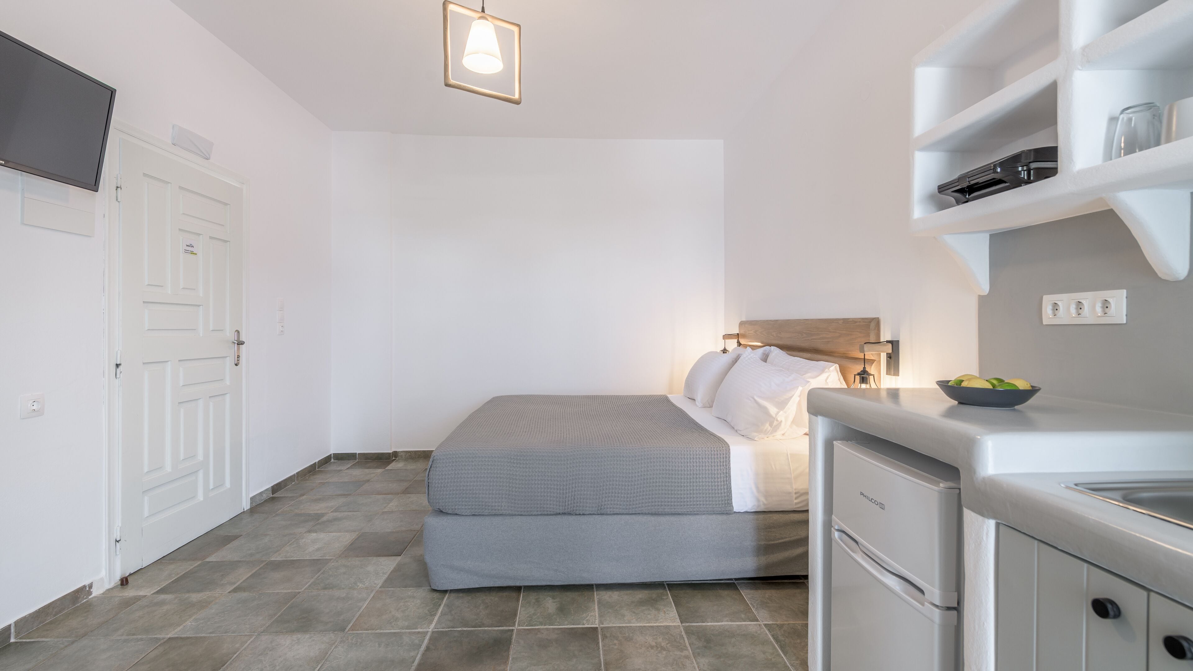 A compact bedroom with a bed, bedside table, and a small kitchenette.