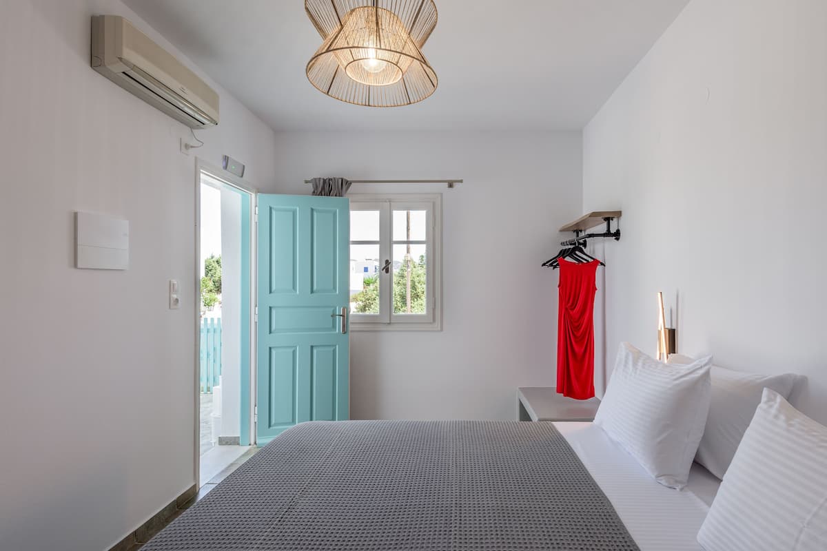 A bedroom with a bed, a window, a door, and a hanging light fixture.