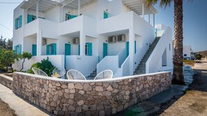 A modern white building with multiple balconies, stone walls, and outdoor seating. - Michalis Studios (Milos)