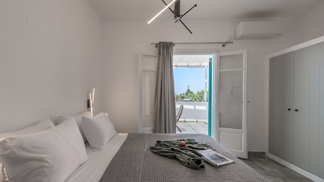 A modern bedroom with a bed, a bedside table, a window with curtains, and an open door leading to a balcony.