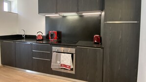 A modern kitchen with dark cabinetry, a stainless steel sink, a kettle, a toaster, and a built-in oven. - Plein centre, T3 5P totalement rénové 55m2. WIFI (Cauterets)