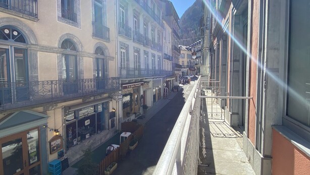 A narrow street with buildings on either side, balconies, and outdoor seating areas. - Plein centre, T3 5P totalement rénové 55m2. WIFI (Cauterets)