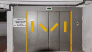 Porta dell'ascensore in metallo con frecce direzionali gialle e un cartello che indica che si tratta di un ascensore senza accelerazione.