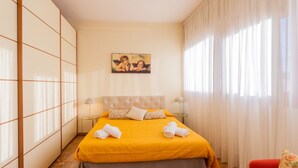 Camera d'albergo con un letto, due lampade ai comodini, un quadro appeso al muro e una finestra con tende.