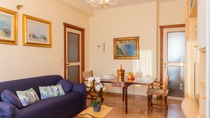 Un soggiorno con un divano blu scuro, un tavolo da pranzo con sedie e un quadro appeso al muro.