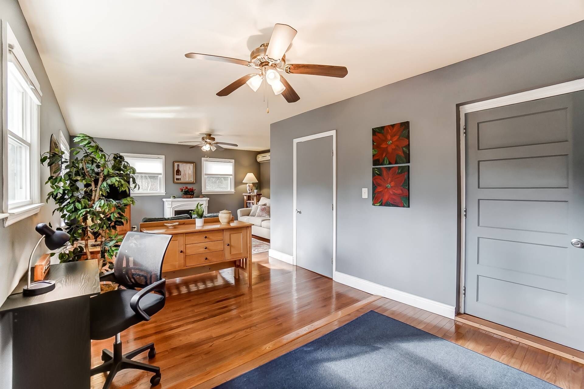 A spacious living room with hardwood floors, a ceiling fan, a dining area with a wooden table and chairs, and a large window.