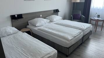 A hotel room with a double bed, a single bed, a small table, a chair, and a lamp.