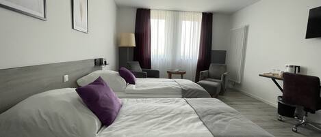 A hotel room with two beds, a desk, a chair, a lamp, and a window with curtains.