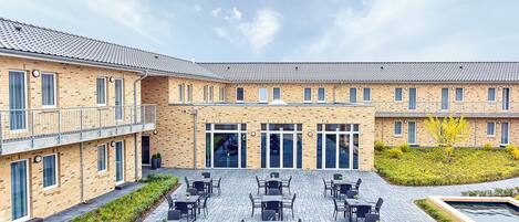 A courtyard with outdoor seating and a brick building with multiple windows and doors.