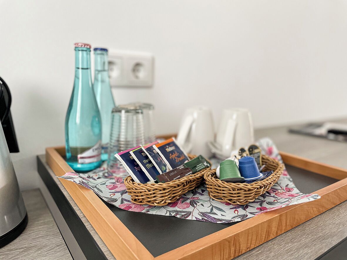 A tray with a wicker basket containing books, a water bottle, and a mug, placed on a floral-patterned mat.