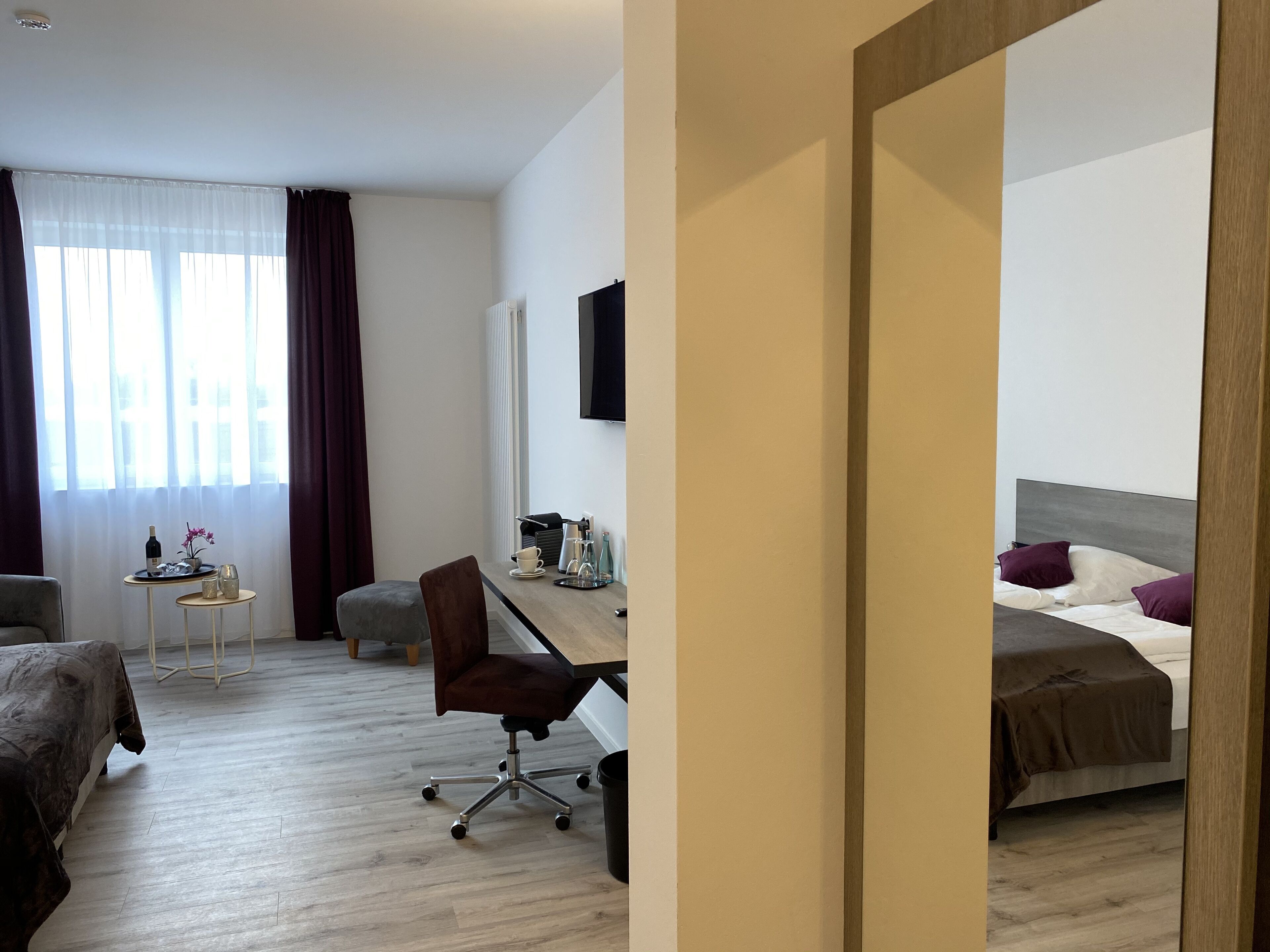 Camera d'albergo con un letto, una scrivania con una sedia, un tavolino con una bottiglia, una tazza e un fiore.