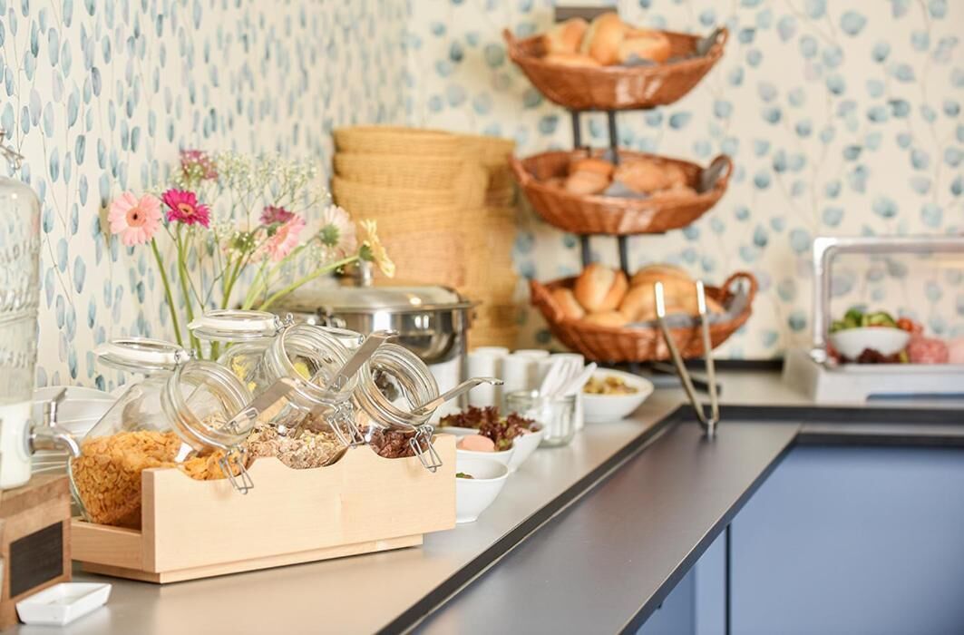 Montaje de un bufé de desayuno con diferentes platillos y un jarrón decorativo con flores.
