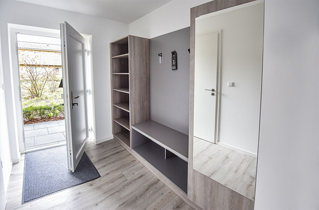 A modern hallway with a sliding door leading to a garden, built-in shelving, and a wardrobe with a mirror.