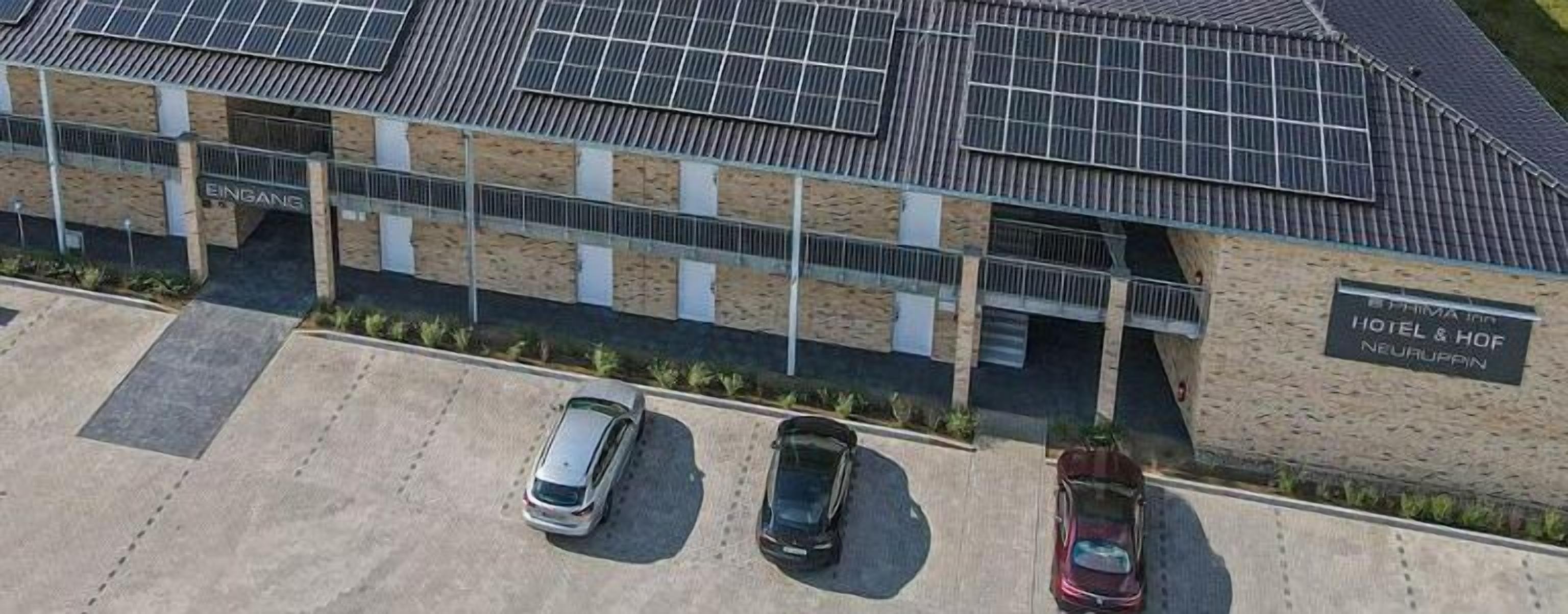 Un hotel de diseño moderno, paneles solares en el techo y un estacionamiento con tres coches.