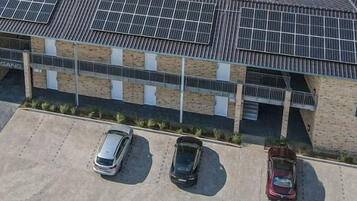 A hotel with a modern design, solar panels on the roof, and a parking lot with three cars.