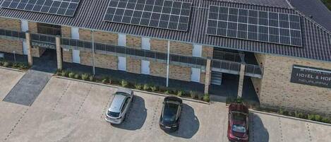 Un hotel de diseño moderno, paneles solares en el techo y un estacionamiento con tres coches.