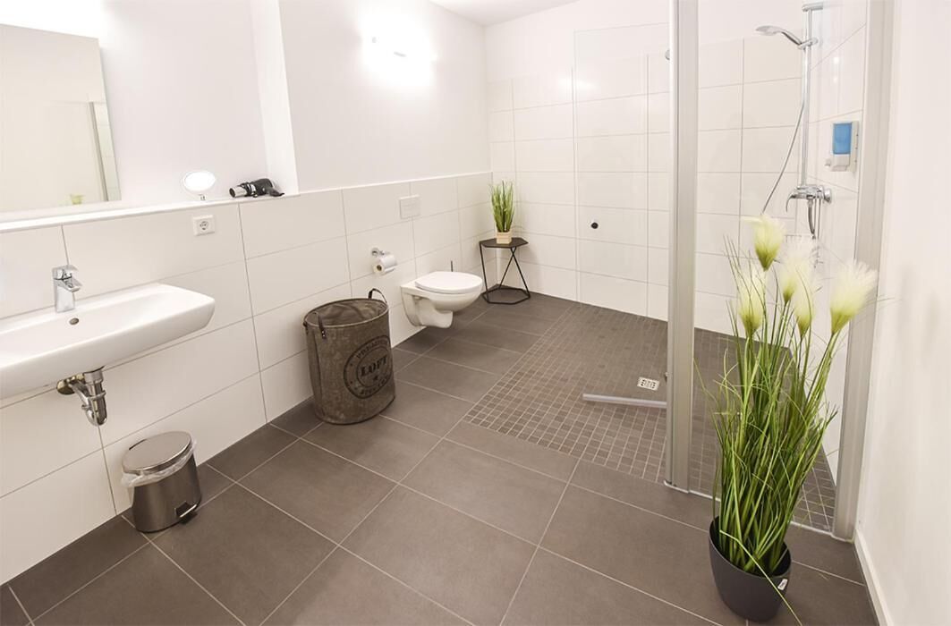Un baño moderno con lavamanos, inodoro y zona de ducha blancos.