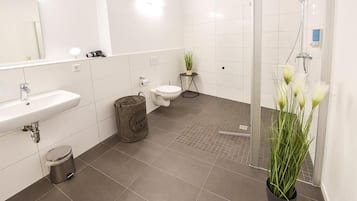 Un baño moderno con lavamanos, inodoro y zona de ducha blancos.
