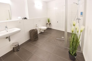 A modern bathroom with a white sink, toilet, and shower area.