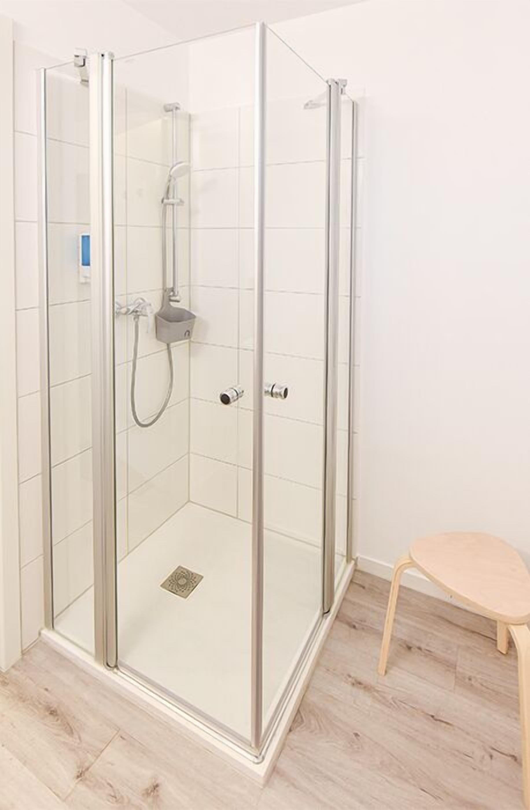 A glass-enclosed shower with a handheld showerhead and a wall-mounted faucet.
