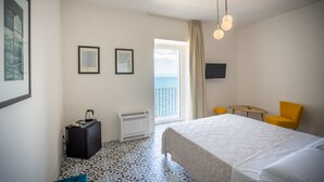 A hotel room with a bed, a desk, a chair, a heater, a suitcase, and a TV on the wall.