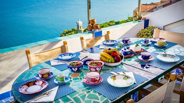 A table set with plates, bowls, and cups, overlooking a body of water.