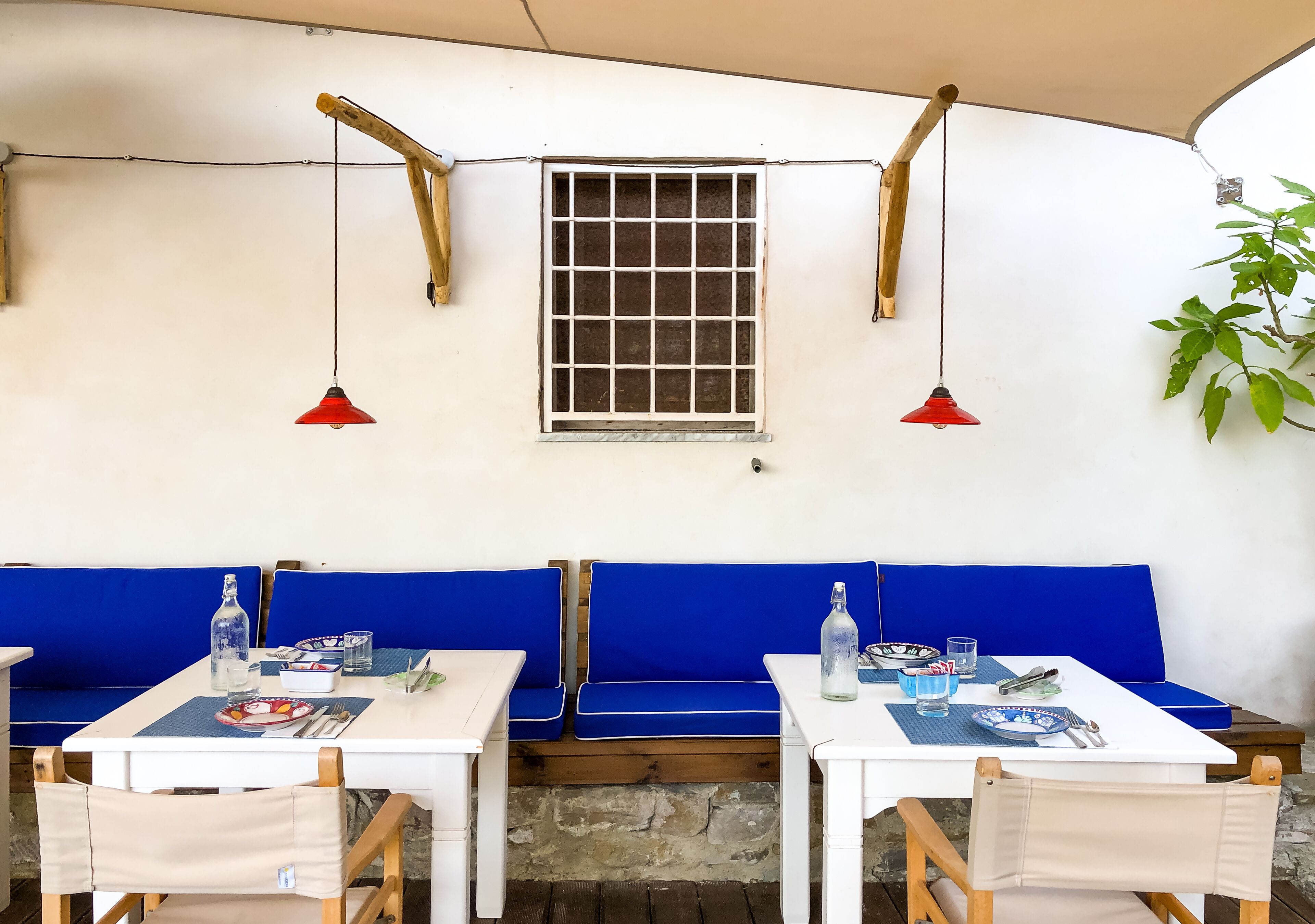 A restaurant with blue cushioned seating, white tables, and red pendant lights.