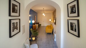 A hallway with framed pictures, a yellow sofa, a green chair, and a patterned chair.