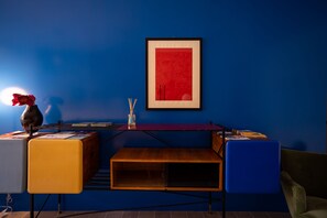 A modern room with a blue wall, a framed red artwork, a wooden desk with a vase, and a blue chair. - Borgo dei Saraceni - Flower Home (Agropoli)