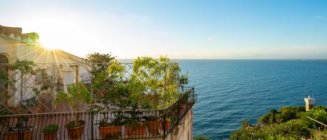 A coastal building with a balcony overlooking the sea, featuring potted plants and a clear view of the ocean.