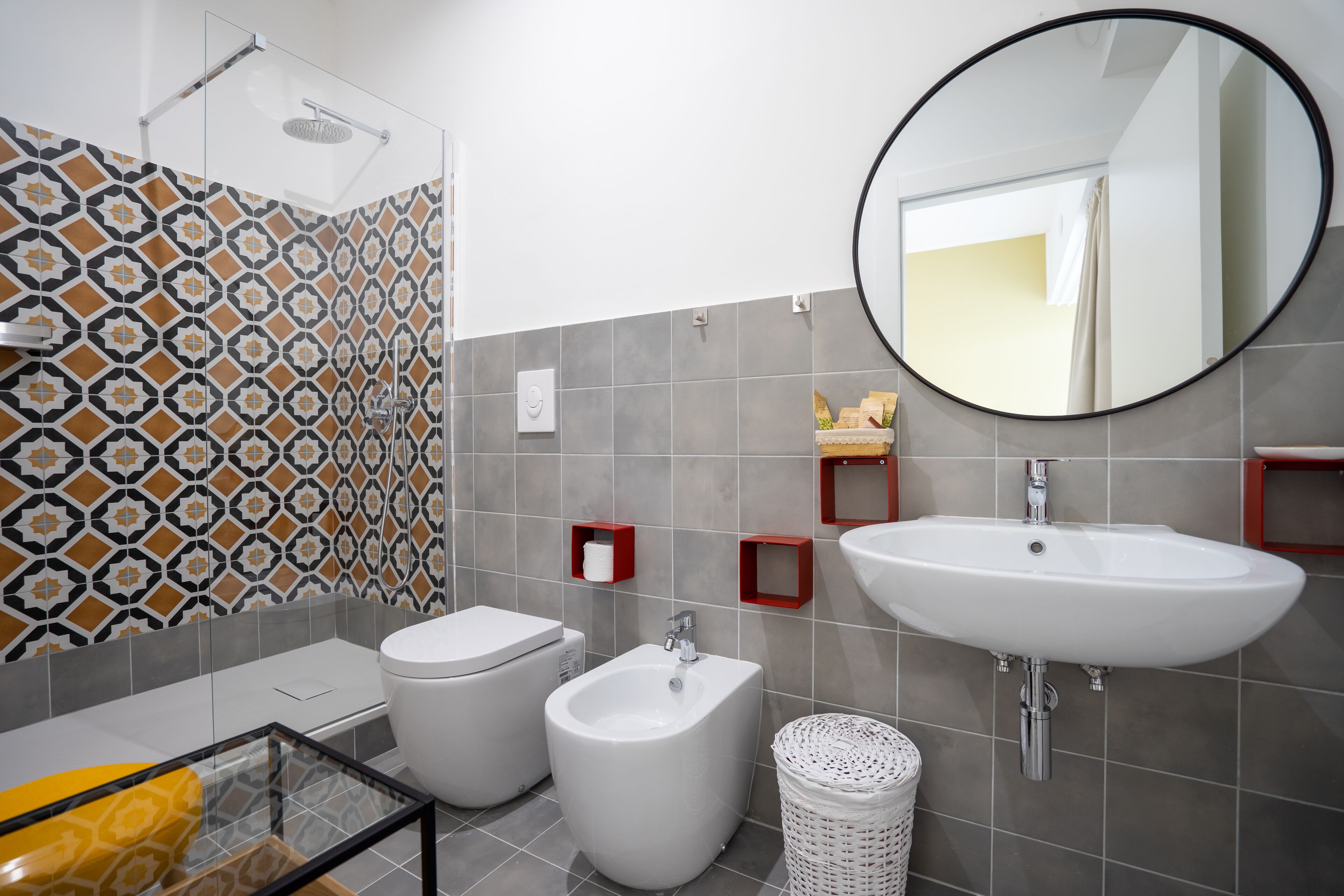 Ein modernes Badezimmer mit einer Duschkabine aus Glas, einem weißen Waschbecken, zwei Bidets und fliesenbesetztem Boden.