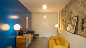 A living room with a yellow sofa, a green armchair, a wooden sideboard, and a stone wall.