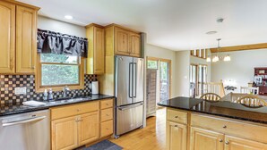 A kitchen with wooden cabinets, a stainless steel refrigerator, and a black countertop. - Mtn Views & Hot Tub: 6-Acre Blue Ridge Retreat! (Swannanoa)