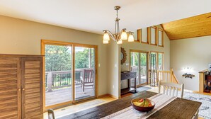 A spacious dining area with a wooden table, a bowl of fruit, and a view to a deck. - Mtn Views & Hot Tub: 6-Acre Blue Ridge Retreat! (Swannanoa)