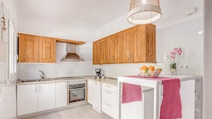 Een moderne keuken met houten kastjes, een ingebouwde oven en een klein eiland met een roze handdoek.