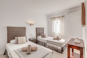 A hotel room with two beds, a nightstand, a wooden table, and a window with curtains.