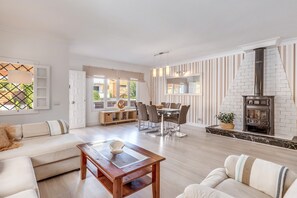 A spacious living area with a sofa, dining table, and chairs, a fireplace, and a view through large windows.