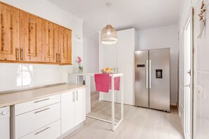 A modern kitchen with white cabinets, a wooden countertop, a stainless steel refrigerator, and a hanging light fixture.