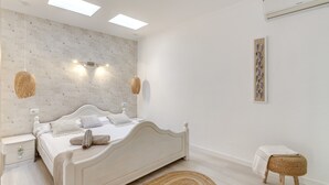 Een slaapkamer met een bed, nachtkastjes, een wandlamp, een geweven kruk en een lijstwerk met een kunstwerk.