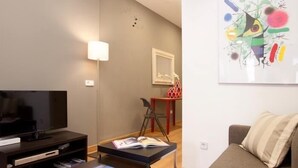 A modern living room with a flat-screen TV, a sofa, a coffee table with books, a floor lamp, and a colorful abstract painting on the wall. - Sagrada Familia - Apartment in Barcelona (Barcelona)