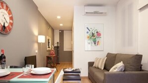 A modern living room with a sofa, a dining table set with plates and glasses, a clock on the wall, and an air conditioning unit. - Sagrada Familia - Apartment in Barcelona (Barcelona)