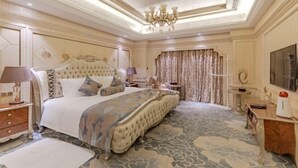Een luxueuze slaapkamer met een groot bed, een kroonluchter en een kamerbreed tapijt met dessin.