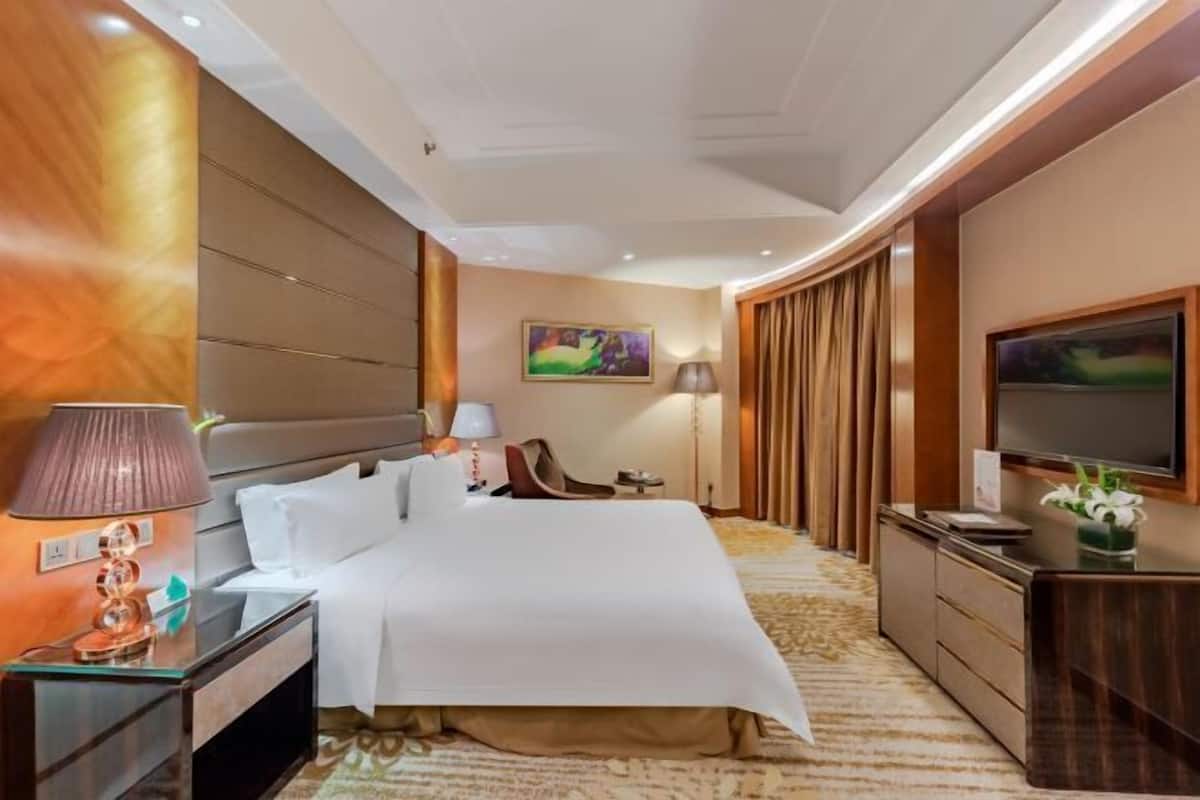 A hotel room with a large bed, a desk with a lamp, a TV, and a painting on the wall.