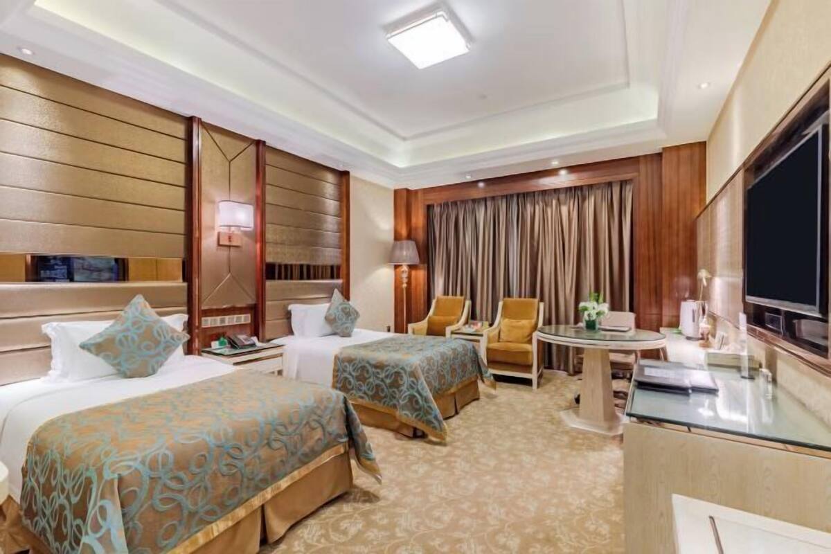 A hotel room with two beds, a TV, a desk, and a chair.