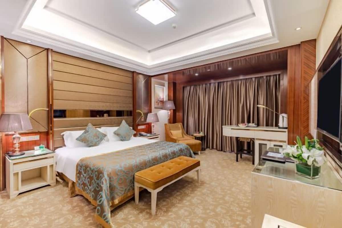 A hotel room with a large bed, a desk, a chair, a TV, and a bathroom.