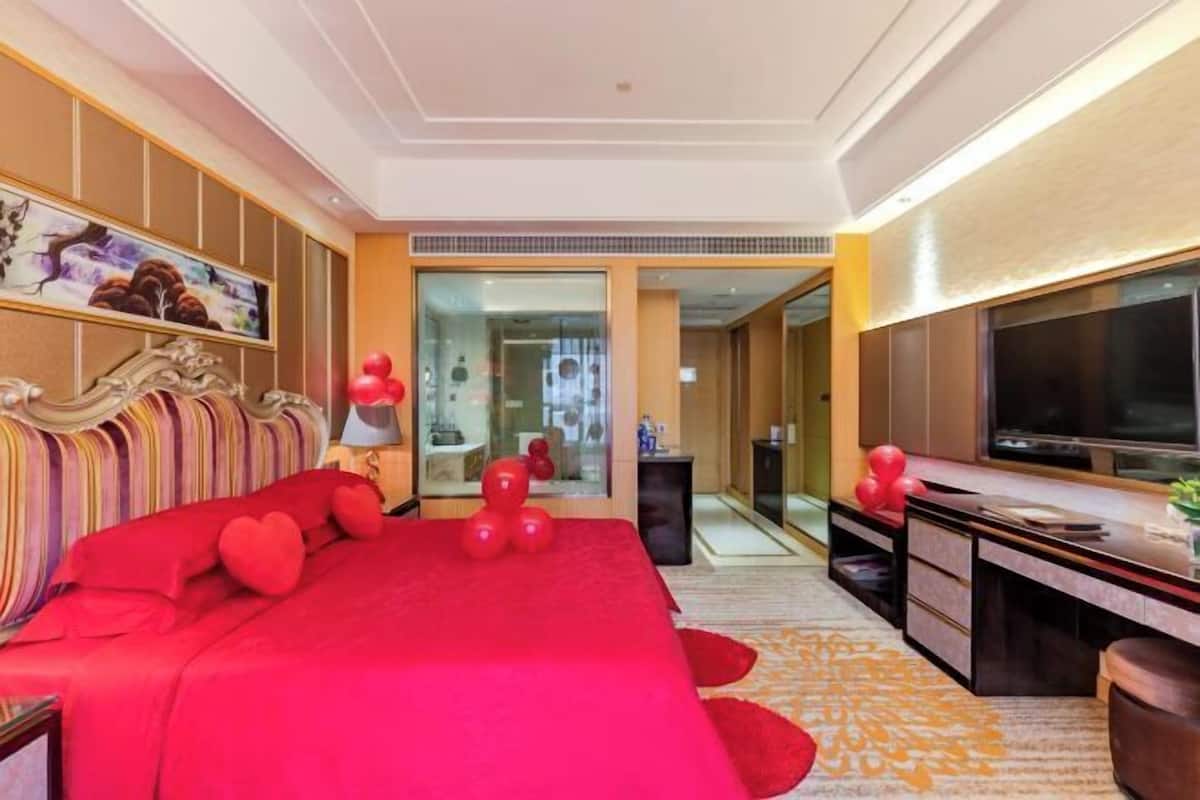 A hotel room with a large bed, a desk, a TV, and a bathroom visible through an open door.