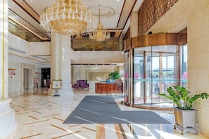 Un vestíbulo de hotel con una recepción, entrada de vidrio y una araña.