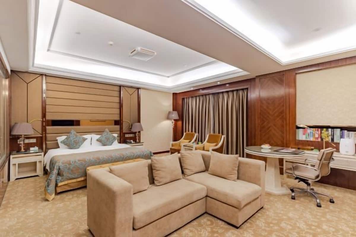 A hotel room with a large bed, a sofa, a desk, and a chair.