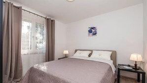Un dormitorio con cama, dos mesitas de noche con lámparas, una ventana con cortinas e imagen colgada en la pared.