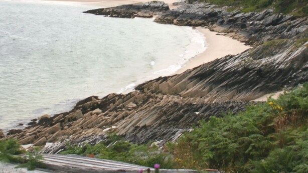 Un paisaje costero con una playa arenosa, acantilados rocosos y vegetación densa.